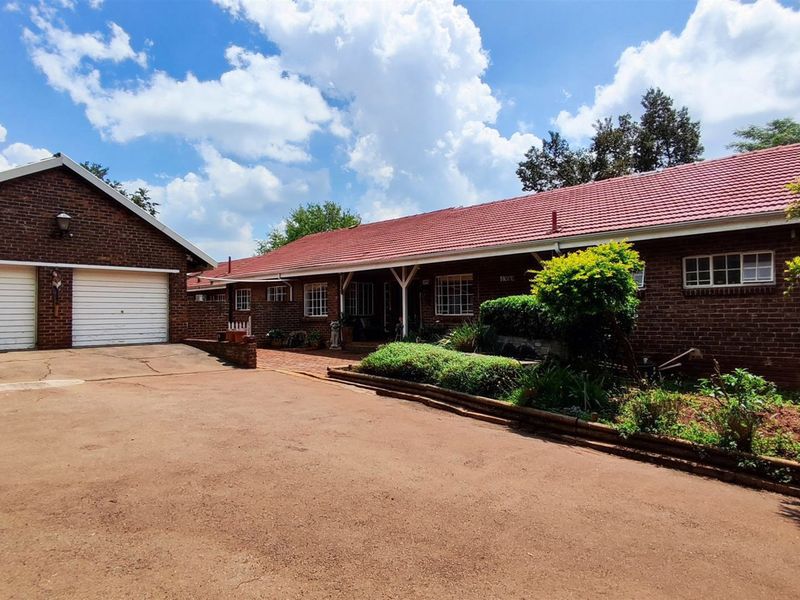 Front view of a brick-faced small holding property featuring a double garage, tiled roof, and a spacious paved driveway area.