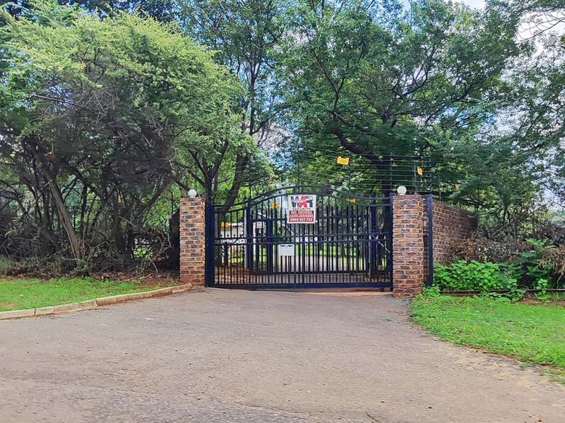 A gated entrance to the property featuring brick pillars, a metal security gate, and electric fencing, set within a mature, tree-lined landscape.
