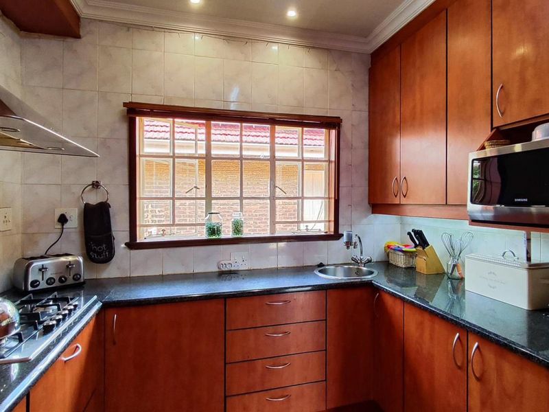 A functional kitchen featuring warm-toned wooden cabinetry, granite countertops, a gas hob with extractor, and a tiled backsplash with a window view.