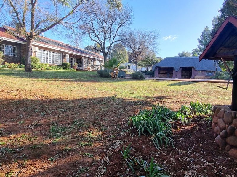 Spacious rear garden featuring a stone-clad wishing well, a thatched lapa entertainment area, and a brick-built main dwelling with solar water heating.