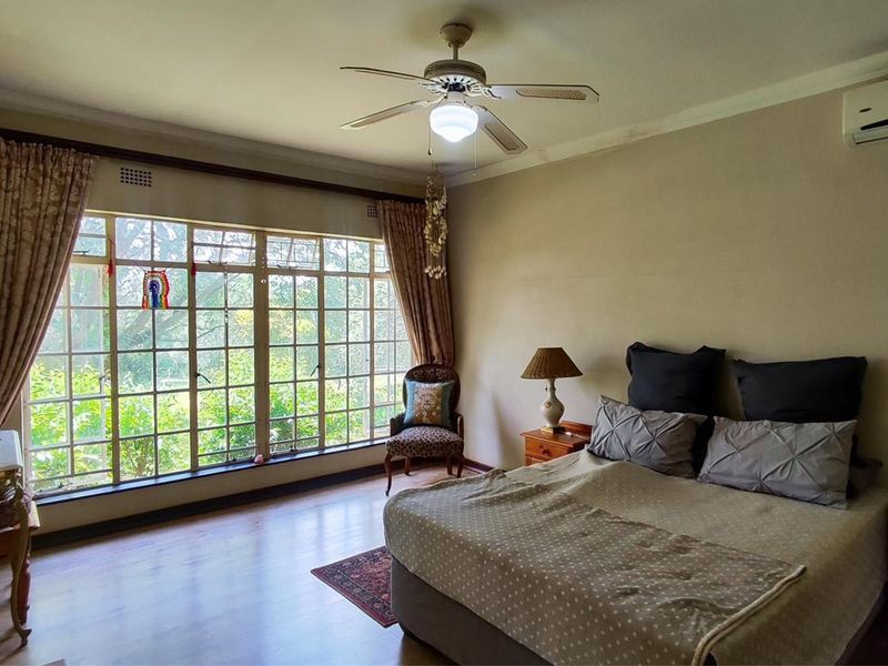 Spacious bedroom featuring large grid-pane windows, laminate flooring, a ceiling fan, and a wall-mounted air conditioning unit.