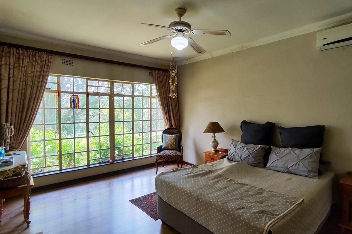 Spacious bedroom featuring large grid-pane windows, laminate flooring, a ceiling fan, and a wall-mounted air conditioning unit.
