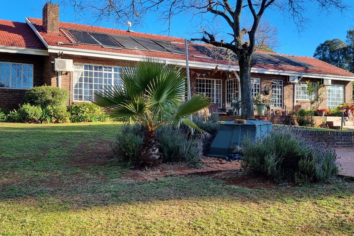 Rear view of a brick-faced small holding residence featuring a tiled roof with solar panels, a swimming pool, and a paved patio area.