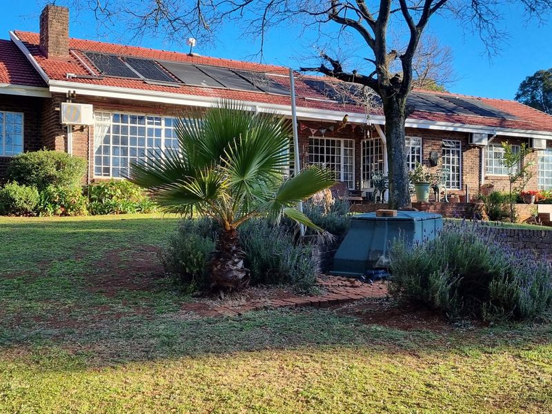 Rear view of a brick-faced small holding residence featuring a tiled roof with solar panels, a swimming pool, and a paved patio area.