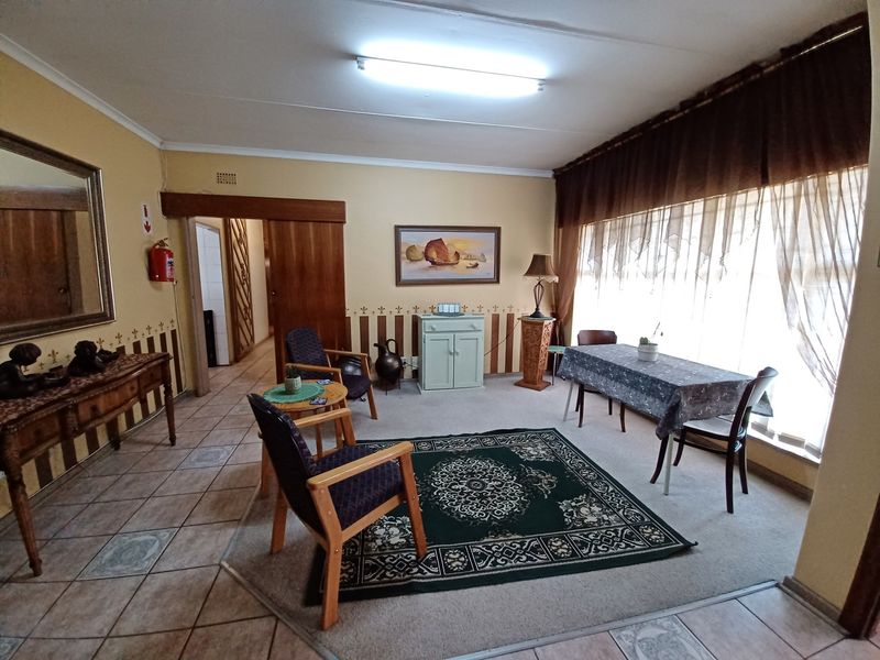 A spacious living area featuring a combination of tiled and carpeted flooring, large windows with curtains, and direct access to an adjacent hallway.