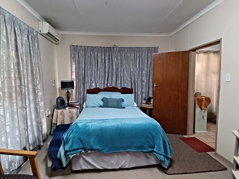 A functional bedroom featuring a wall-mounted air conditioning unit, neutral wall finishes, and direct access to an adjoining bathroom.