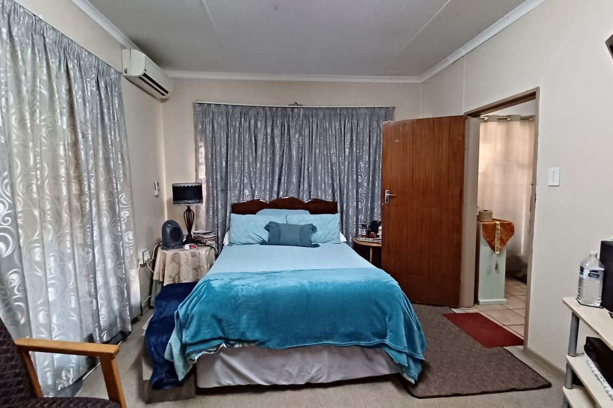 A functional bedroom featuring a wall-mounted air conditioning unit, neutral wall finishes, and direct access to an adjoining bathroom.