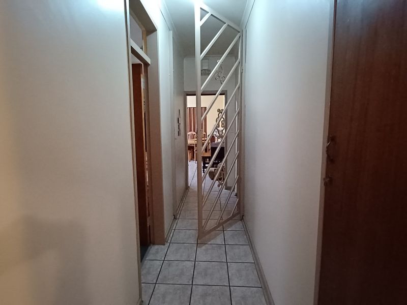 A functional hallway featuring tiled flooring, a security gate, and built-in storage cupboards, providing access to other areas of the home.