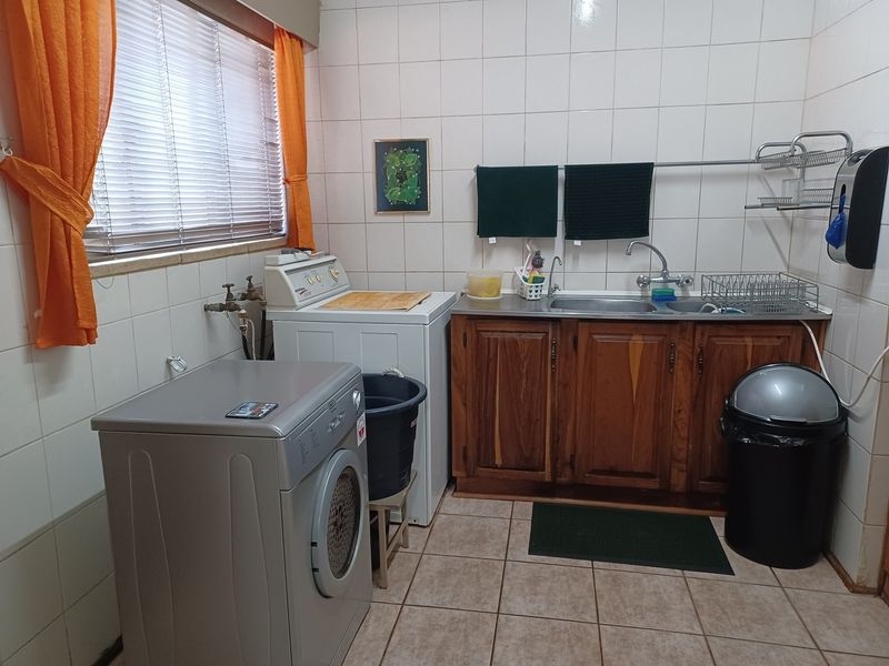 A functional laundry room featuring tiled walls and flooring, wooden cabinetry, a stainless steel sink, and dedicated plumbing connections for appliances.