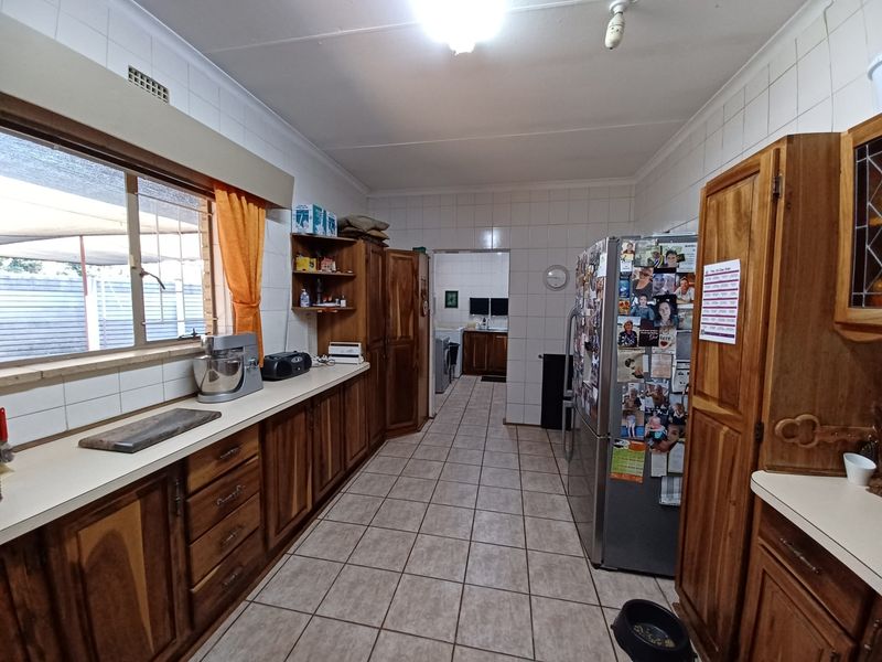 A functional kitchen featuring wooden cabinetry, tiled walls, and tiled flooring, with a view through to an adjacent utility area.