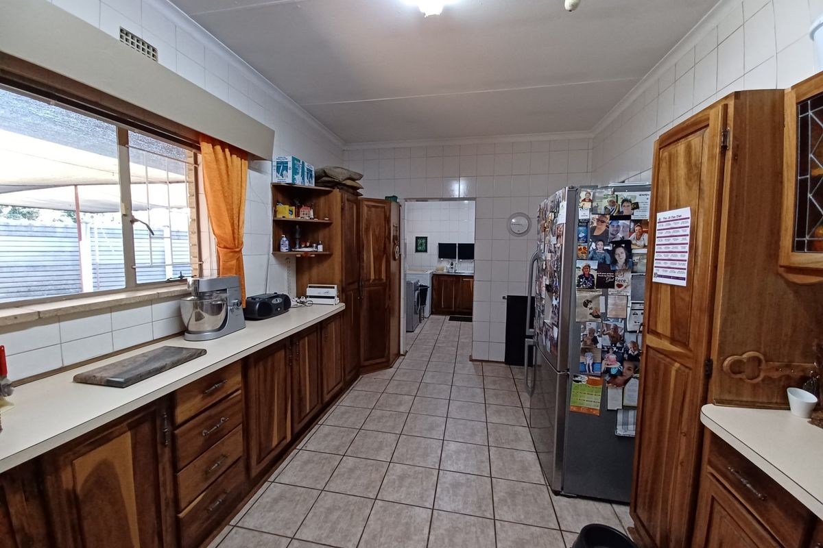 A functional kitchen featuring wooden cabinetry, tiled walls, and tiled flooring, with a view through to an adjacent utility area.