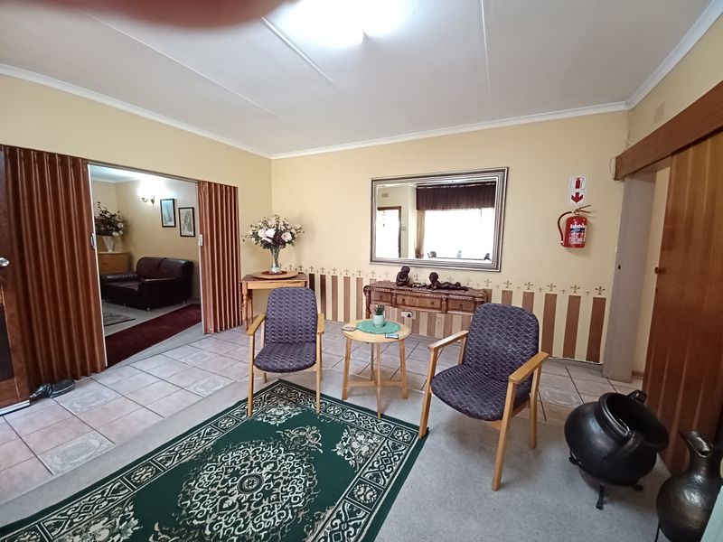A living room featuring tiled flooring, a folding room divider, and a wall-mounted fire extinguisher, with dated wall finishes and decor.