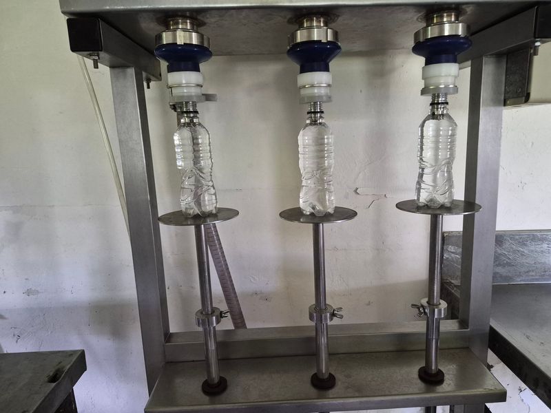 A close-up view of an industrial bottling machine used for liquid packaging, featuring a stainless steel frame and multiple filling stations.