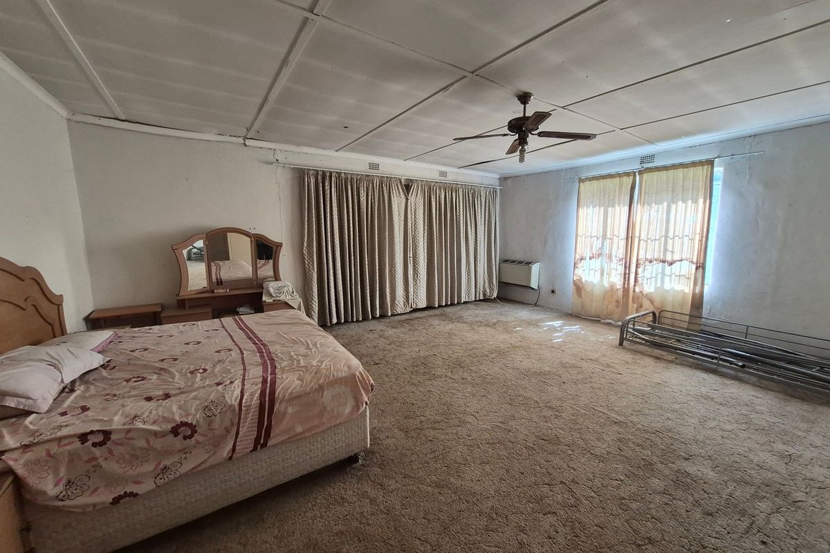 Spacious bedroom featuring a ceiling fan, wall-mounted air conditioning unit, and carpeted flooring, requiring cosmetic updates to improve its overall condition.