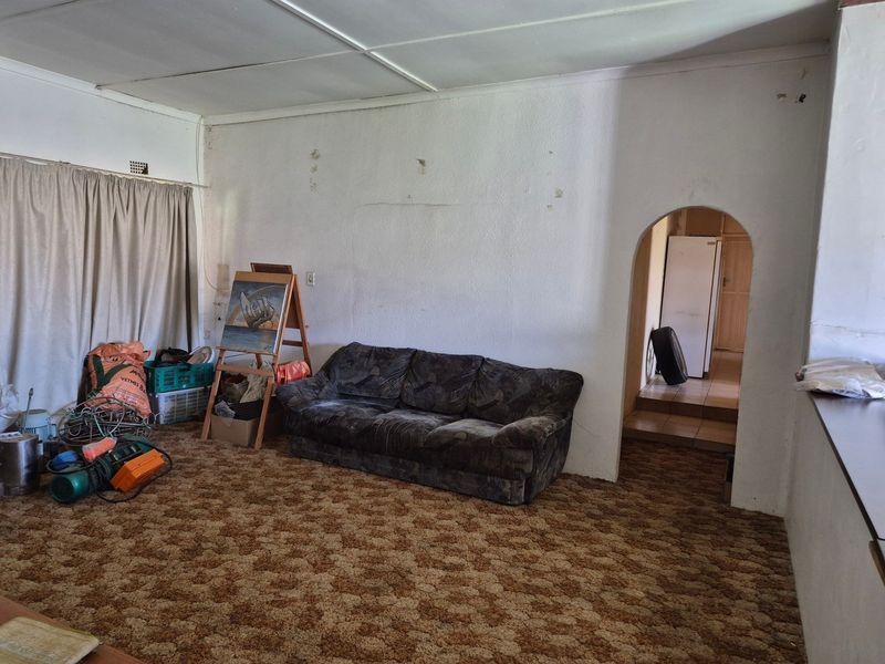 A living room area featuring an arched doorway leading to an adjacent space, with dated carpet flooring and walls requiring maintenance and cosmetic updates.