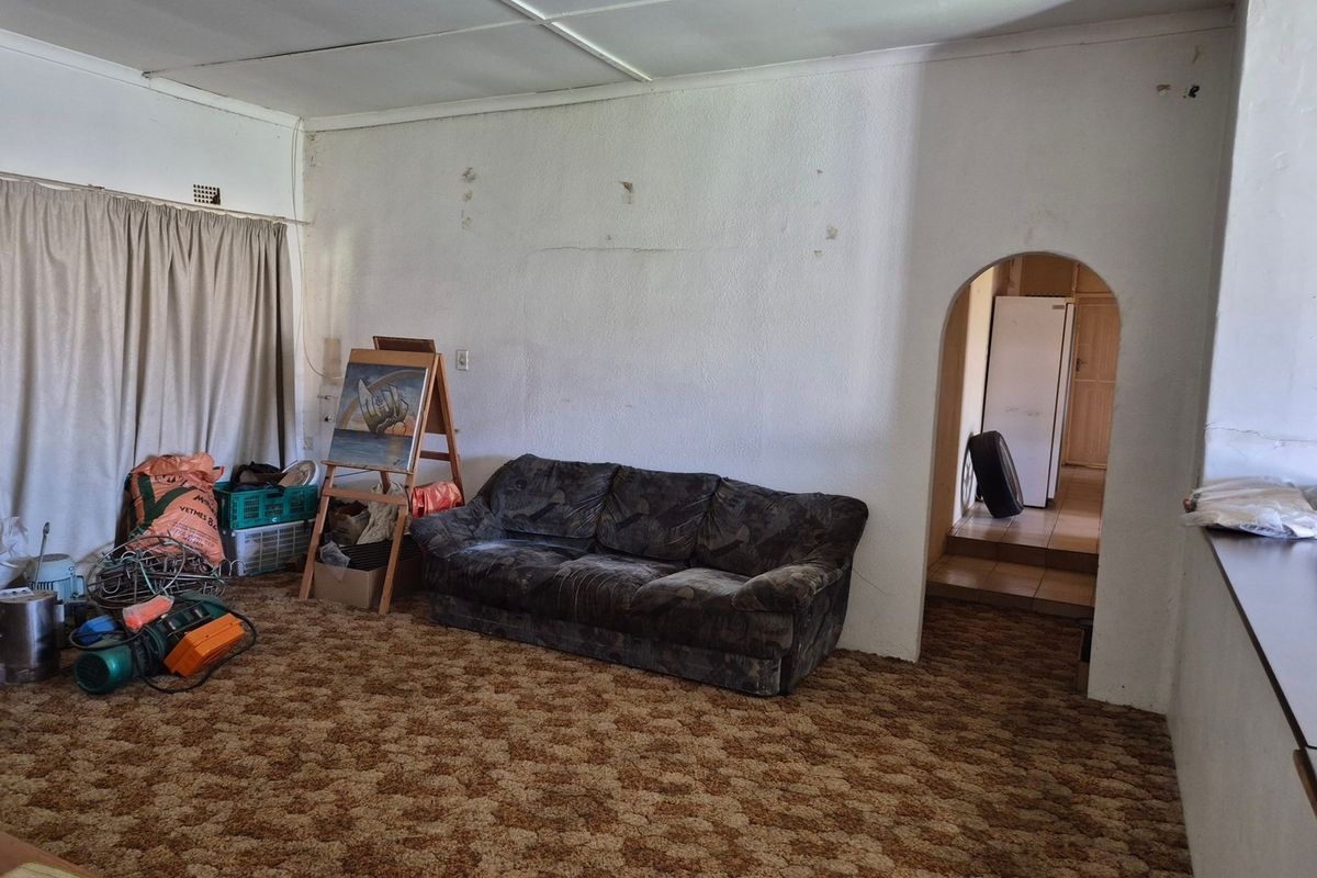 A living room area featuring an arched doorway leading to an adjacent space, with dated carpet flooring and walls requiring maintenance and cosmetic updates.