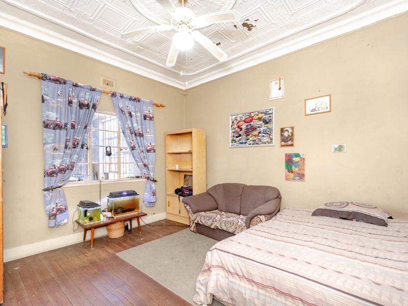 A bedroom featuring original pressed metal ceilings, timber flooring, and security bars on the window. The ceiling shows signs of paint deterioration.