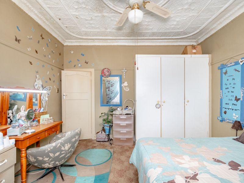 A bedroom featuring a classic ornate pressed metal ceiling, a ceiling fan, and a built-in wardrobe, requiring cosmetic updates to the walls and flooring.