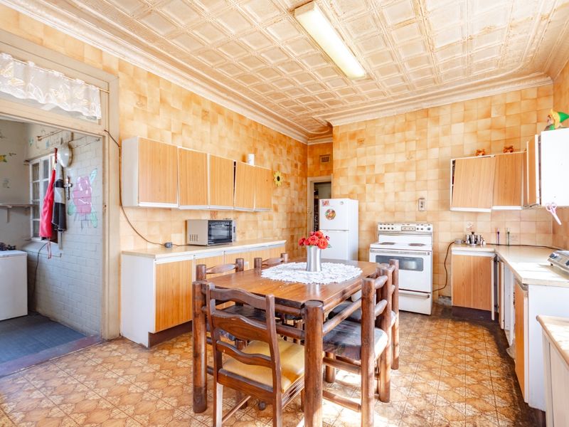A dated kitchen featuring original wall and floor tiles, decorative ceiling panels, and built-in cabinetry, offering significant potential for a modern renovation.