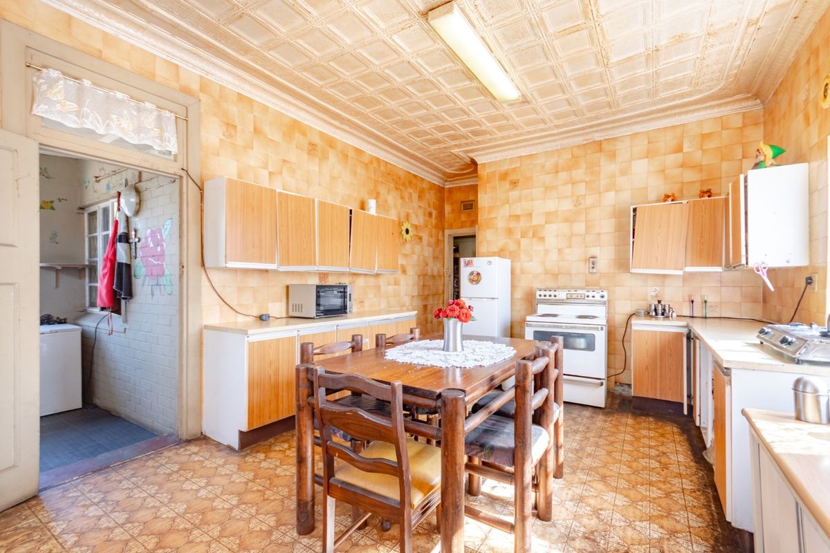 A dated kitchen featuring original wall and floor tiles, decorative ceiling panels, and built-in cabinetry, offering significant potential for a modern renovation.