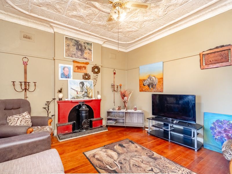 A character-filled living room featuring original pressed metal ceilings, hardwood flooring, and a traditional fireplace, offering a warm and historic atmosphere.