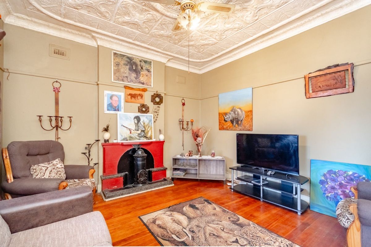 A character-filled living room featuring original pressed metal ceilings, hardwood flooring, and a traditional fireplace, offering a warm and historic atmosphere.