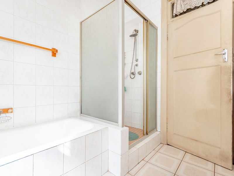 A functional bathroom featuring a built-in bathtub, a separate shower enclosure with a glass door, and tiled surfaces throughout.