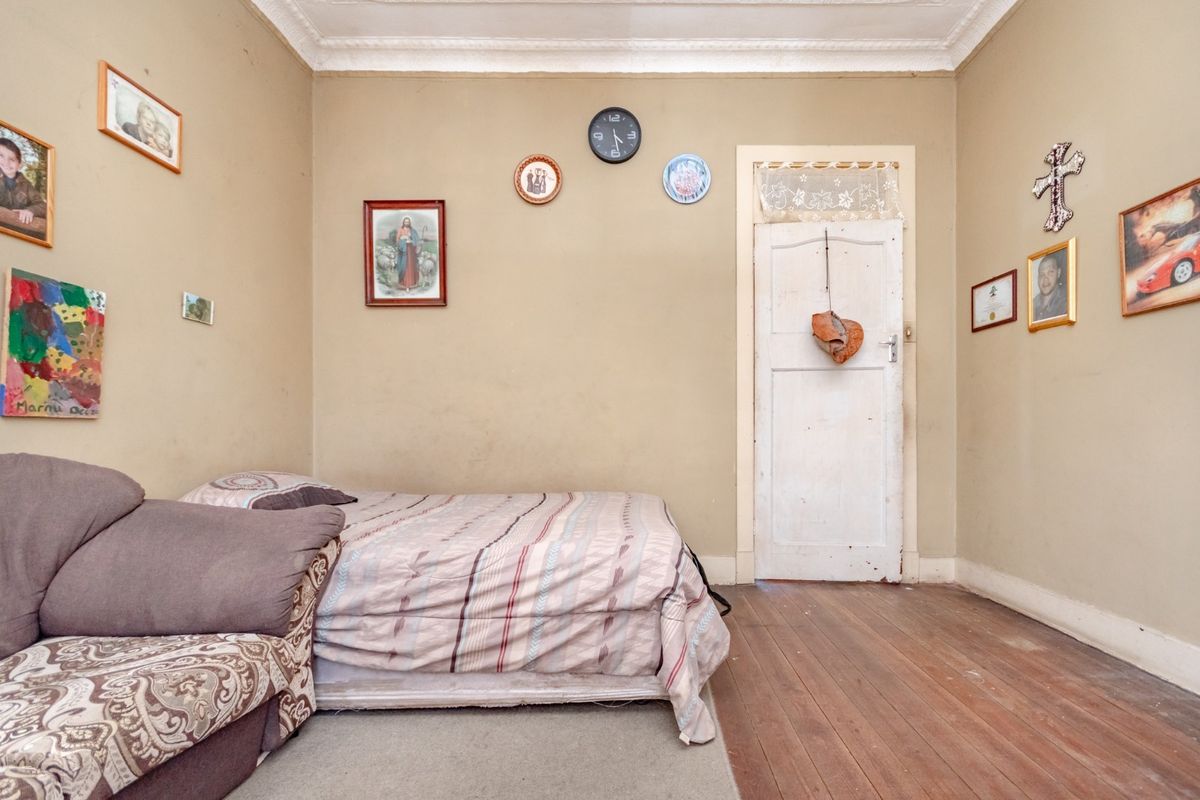 A bedroom featuring original timber flooring, decorative ceiling cornicing, and a traditional timber door with a transom window.