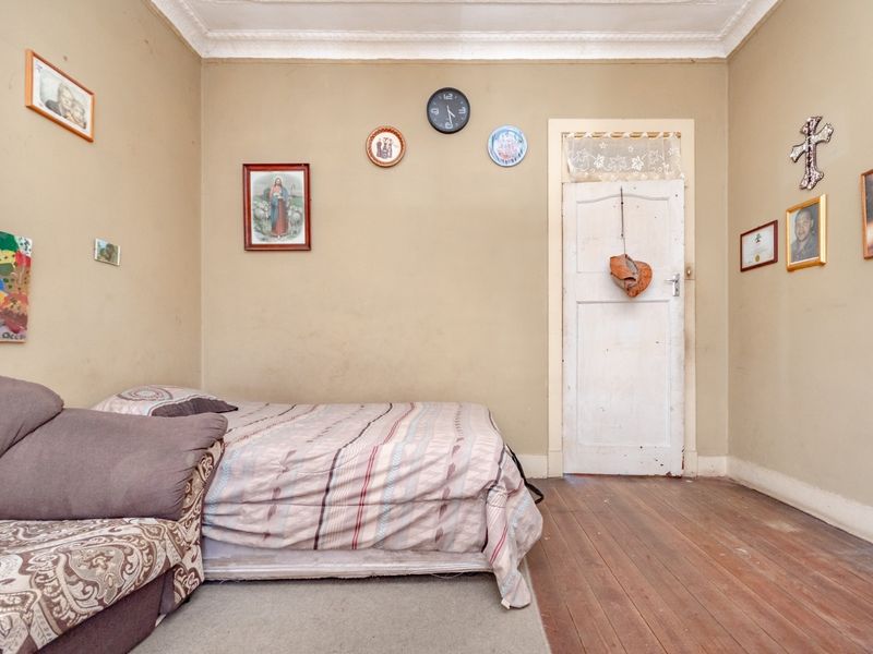 A bedroom featuring original timber flooring, decorative ceiling cornicing, and a traditional timber door with a transom window.
