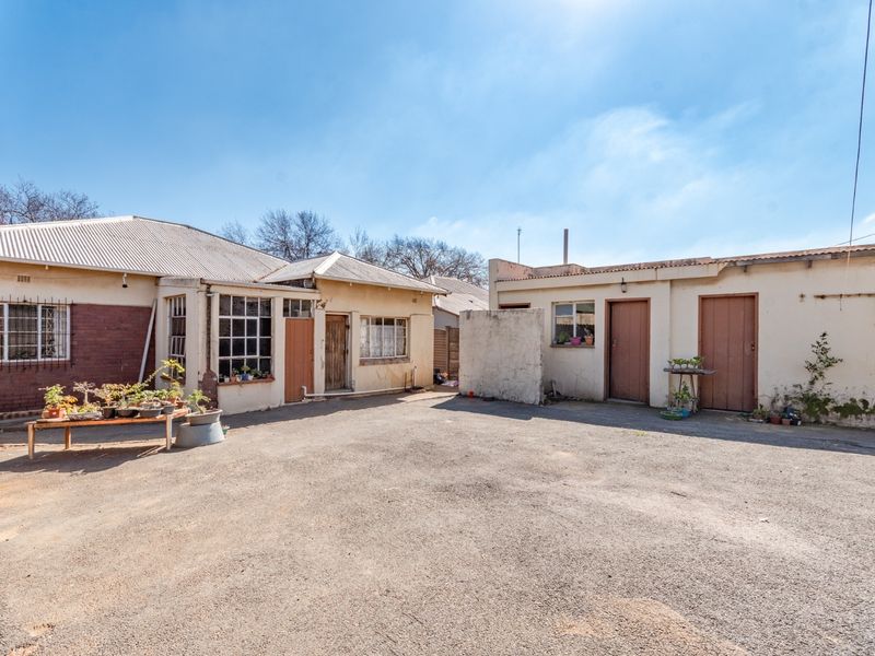 Rear exterior view of the property featuring an asphalt courtyard, multiple access doors, and original steel-framed windows with security bars.