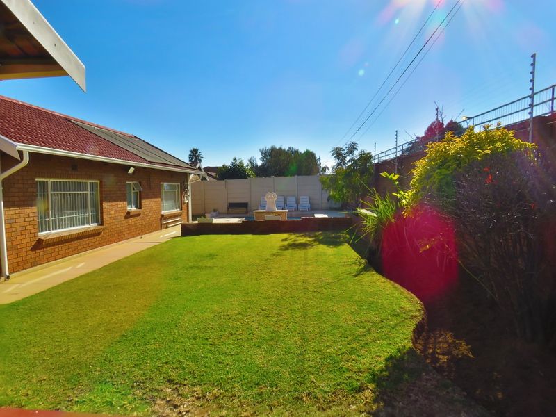 Rear garden view featuring a brick house, a well-maintained lawn, and a swimming pool area enclosed by a perimeter wall with electric fencing.