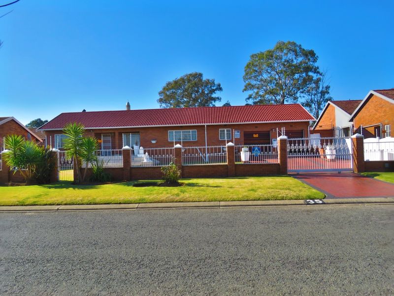 Front view of a well-maintained single-story brick house featuring a red tiled roof, secure perimeter fencing, and a paved driveway leading to a double garage.