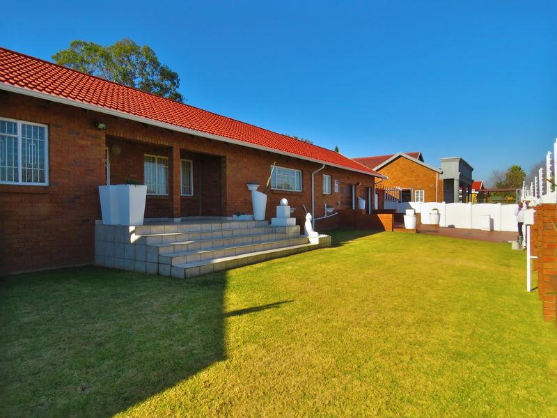 A rear view of a face brick house featuring a red tiled roof, a raised tiled patio area, and a well-maintained lawn.
