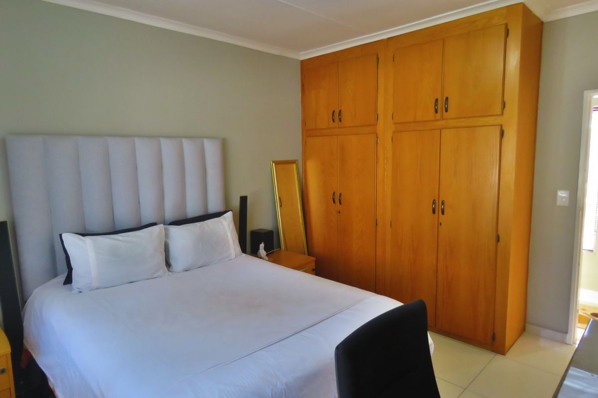 A bedroom featuring built-in wooden cupboards, tiled flooring, and a coved ceiling, offering a functional and neutral living space.