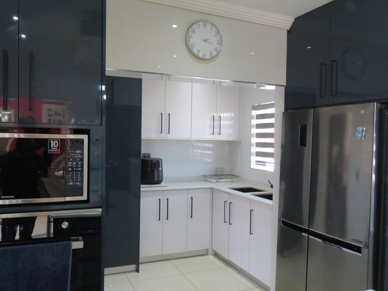 Modern kitchen featuring high-gloss dark and white cabinetry, integrated appliances, quartz countertops, and tiled flooring.