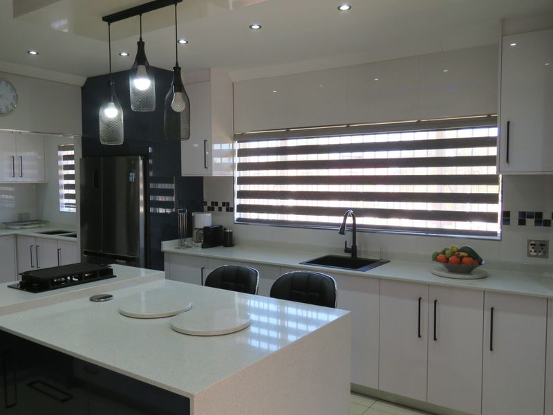 Modern kitchen featuring high-gloss white cabinetry, stone countertops, a central island, and contemporary pendant lighting with integrated sink and cooktop.
