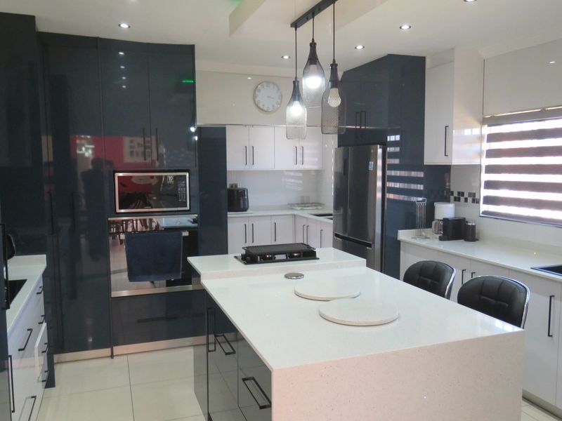 Modern kitchen featuring high-gloss dark cabinetry, a central island with quartz countertops, built-in appliances, and contemporary pendant lighting.