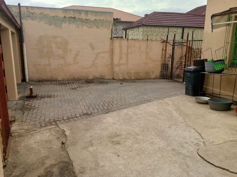 A paved and concrete rear courtyard area enclosed by perimeter walls with security razor wire and a metal gate.