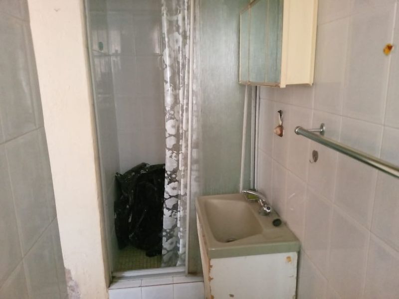 A dated bathroom featuring a shower enclosure, vanity basin, and wall-mounted cabinet, requiring cosmetic updates and repairs to finishes.