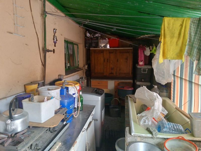 A functional laundry and utility area featuring built-in cabinetry, a utility sink, and exposed plumbing under a corrugated roof structure.