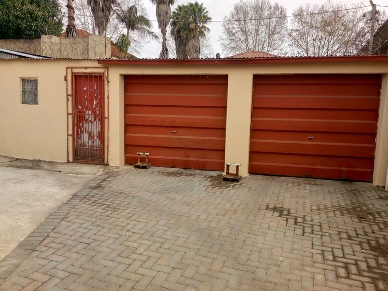 A double garage with red metal doors and a side security gate, featuring a paved driveway and perimeter walling with security wire.