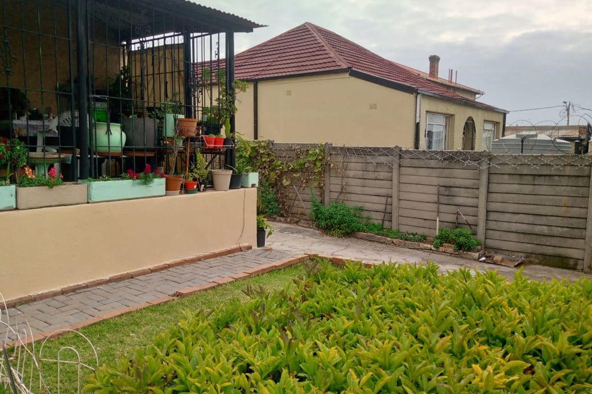 Rear garden area featuring a paved walkway, a covered patio with security gates, and a precast concrete boundary wall with security spikes.