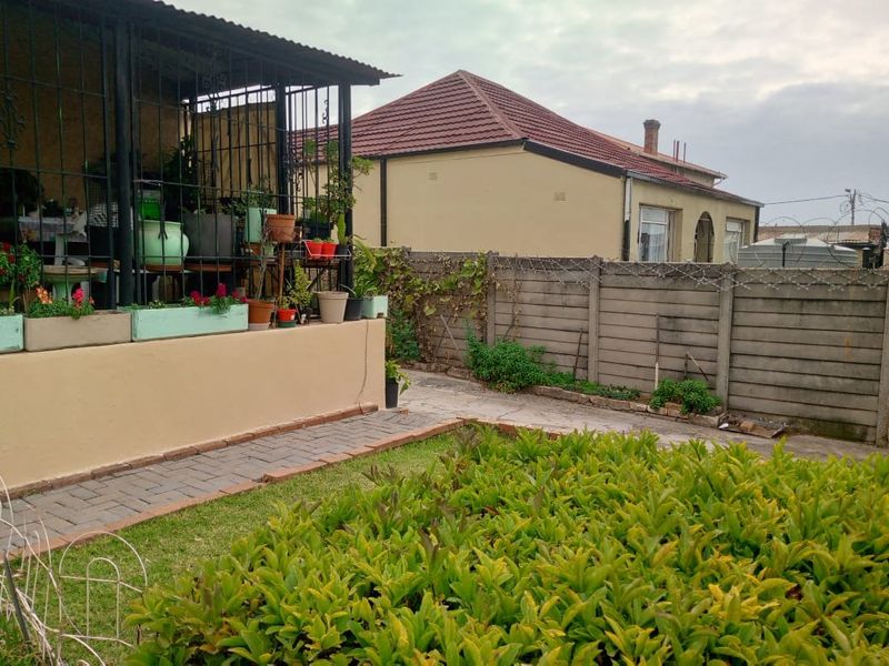 Rear garden area featuring a paved walkway, a covered patio with security gates, and a precast concrete boundary wall with security spikes.