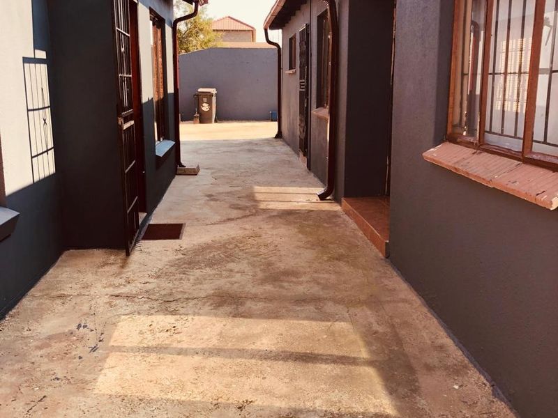 A narrow paved side passage between two building structures featuring security gates and metal window bars.