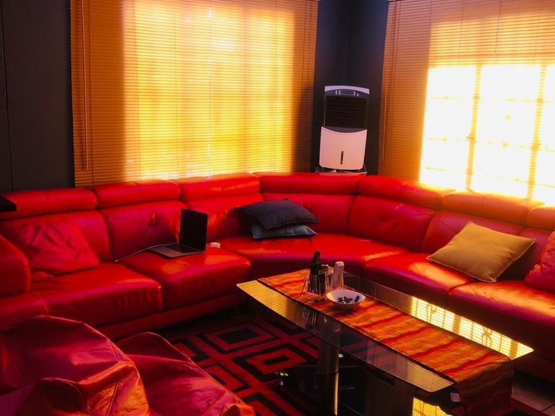 A living room featuring tiled flooring, decorative ceiling cornices, and a ceiling-mounted projector, illuminated by natural light through venetian blinds.