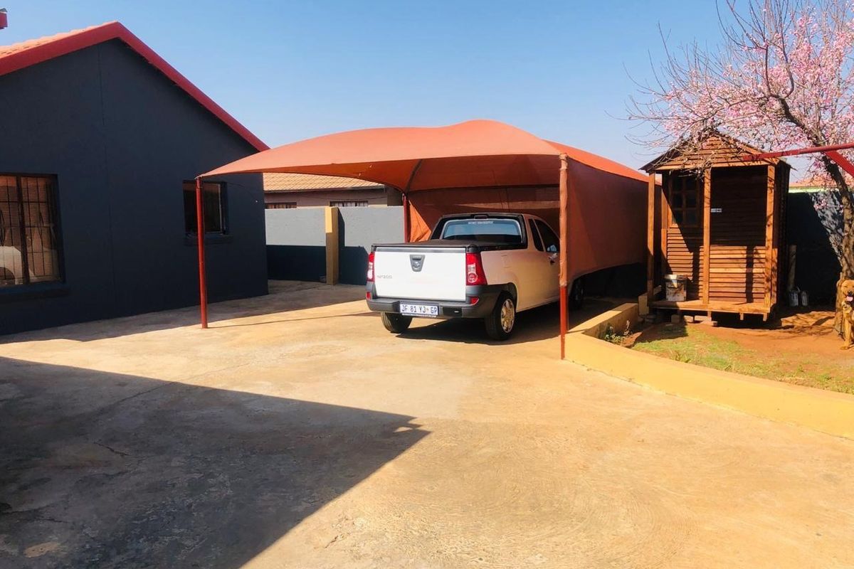Rear exterior area featuring a concrete driveway, a shade cloth carport structure, and a small timber garden shed.