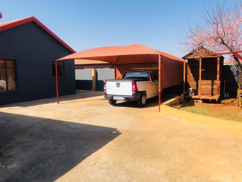 Rear exterior area featuring a concrete driveway, a shade cloth carport structure, and a small timber garden shed.