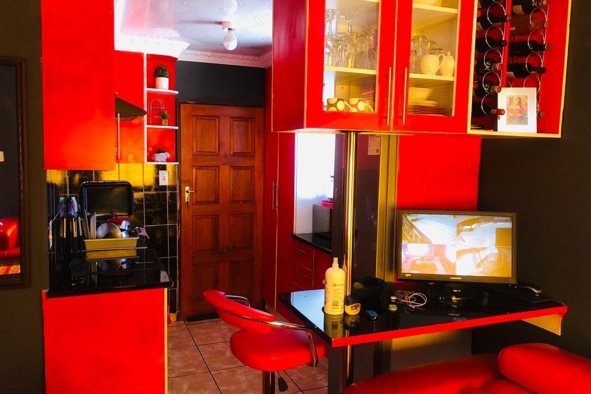 Compact kitchen featuring vibrant red cabinetry, a built-in breakfast bar, wine storage, and tiled flooring with a traditional wooden door.