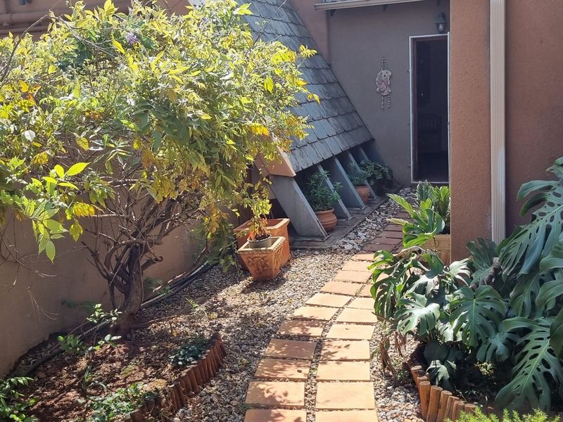 A rear garden area featuring a stone-tiled pathway, gravel landscaping, and a unique sloped architectural roof feature leading to an exterior entrance.
