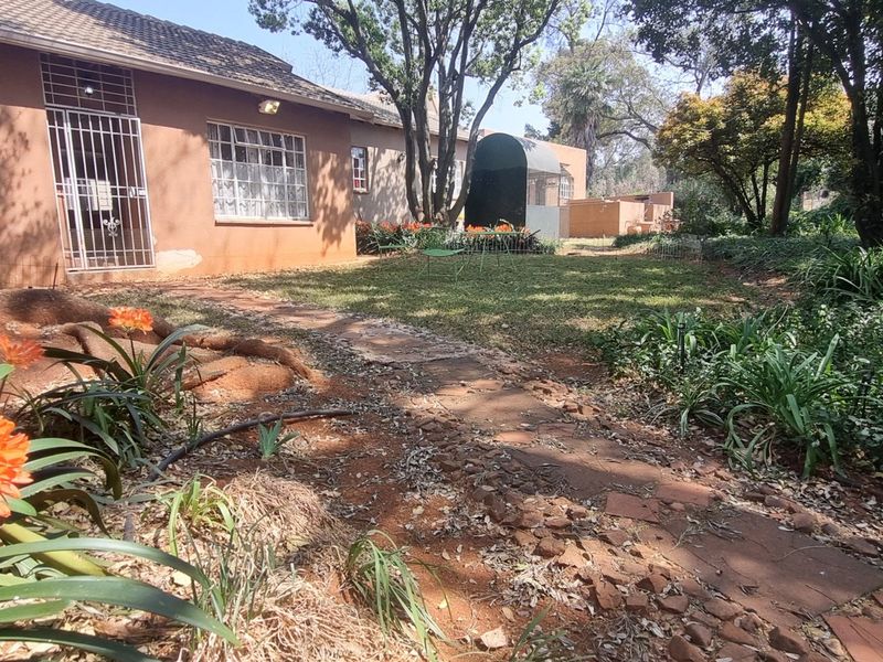 Rear view of the property showing a garden area, paved walkway, and exterior building facade with security features.